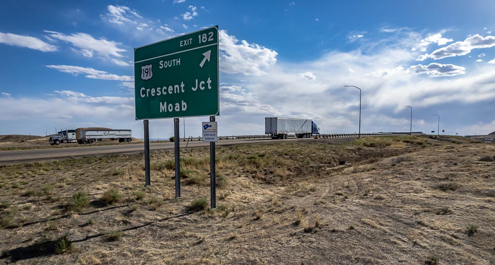 highway sign marks exit 182 off Highway 191, toward Moab and Crescent Junction, as two semis drive past