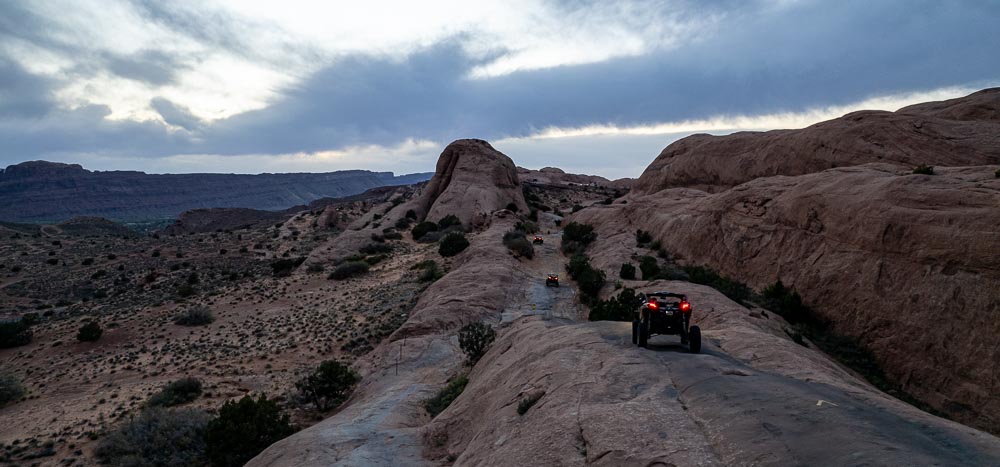 three off-highway vehicles make an evening drive through the start of Hell's Revenge in Sand Flats Recreation Area near Moab, Utah