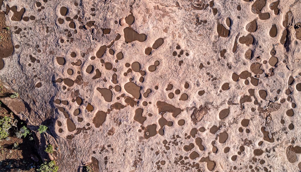 circular puddles of sandy water sit in on red sandstone