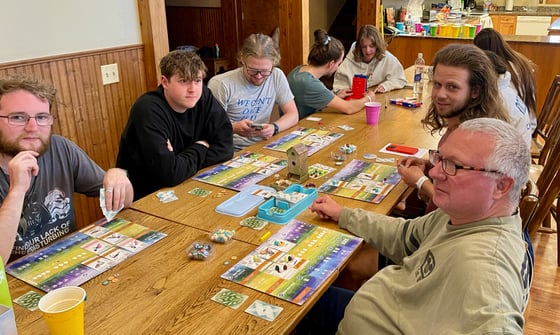 five guys sit around a board game with birds, eggs, cards, a tiny birdhouse, and other bird-themed game pieces