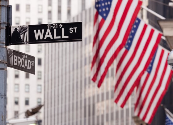 American flags wave behind the street signs in New York, New York for Wall St. and Broad St.